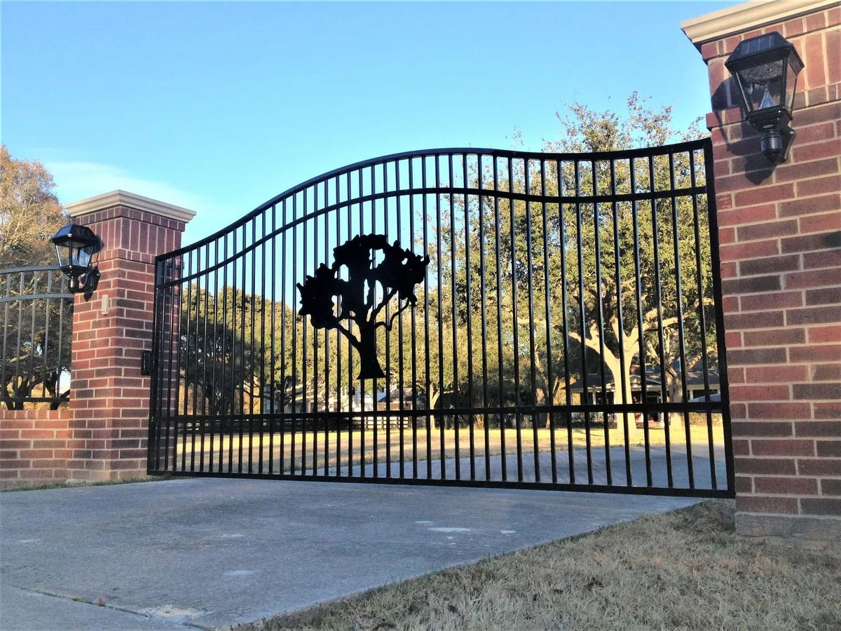 A custom iron driveway gate with a plasma-cut oak silhouette, built by Texas Fence